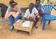 Aperçu Varinia Dieperink, coopérante d’Eirene Suisse en Ouganda, avec un enfant dont l’écolage était financé par l’un des projets de YOLRED, en train d’écrire une lettre de remerciements. source Photo : Varinia Dieperink, Eirene Suisse
