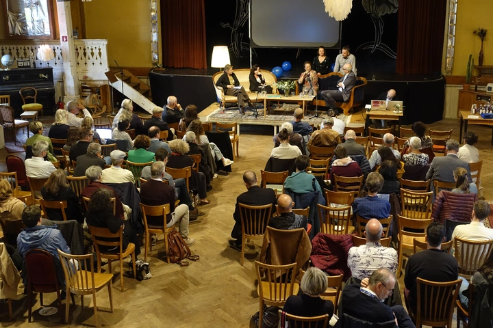 Bild des Saals mit Podiumsdiskussion und Gästen