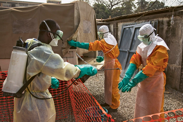 Ein Mitarbeiter des Roten Kreu­zes desinfiziert in Conakry die Handschuhe eines Kollegen mit einer Chlorlösung. Zwischen 2014 und 2016 gehörte Guinea zu den Ländern, die am stärksten vom Ebola-Ausbruch betroffen waren. Foto: UN Photo/Martine Perret