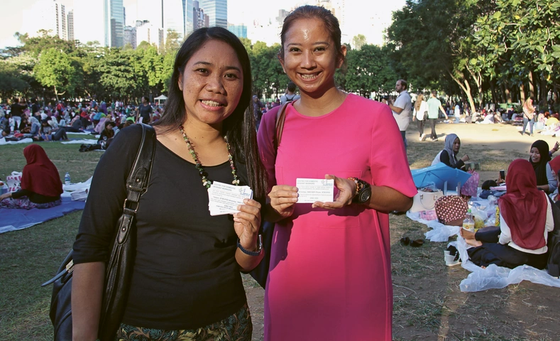 Vivi Wangka und ihre Mitarbeiterin vom Rechtsberatungsdienst verteilen im Hongkonger Victoria Park Visitenkarten und erklären den Hausangestellten, in welchen Fällen sie bei ihnen Unterstützung erhalten. Quelle Foto: Mission 21