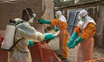 Ein Mitarbeiter des Roten Kreu­zes desinfiziert in Conakry die Handschuhe eines Kollegen mit einer Chlorlösung. Zwischen 2014 und 2016 gehörte Guinea zu den Ländern, die am stärksten vom Ebola-Ausbruch betroffen waren. Foto: UN Photo/Martine Perret