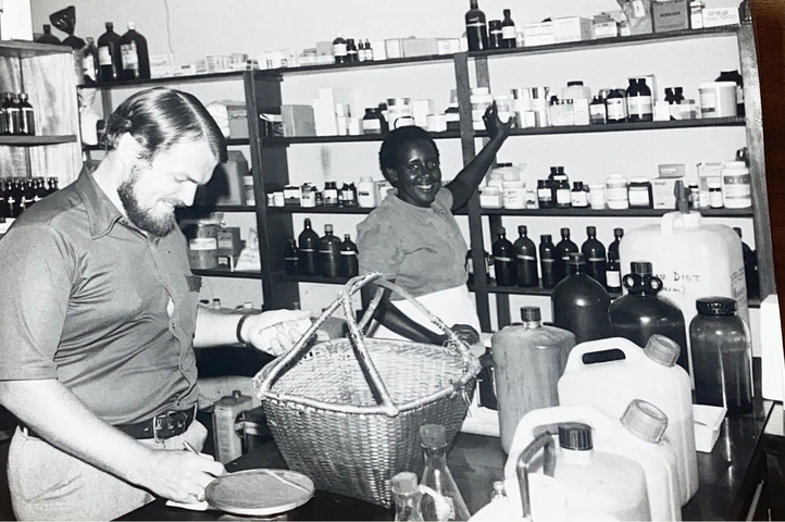 Dr Watt, pharmacien en affectation auprès du Service de Missions et d’Entraide en République démocratique du Congo, à la pharmacie avec une aide citoyenne. Photo: SME (1983).