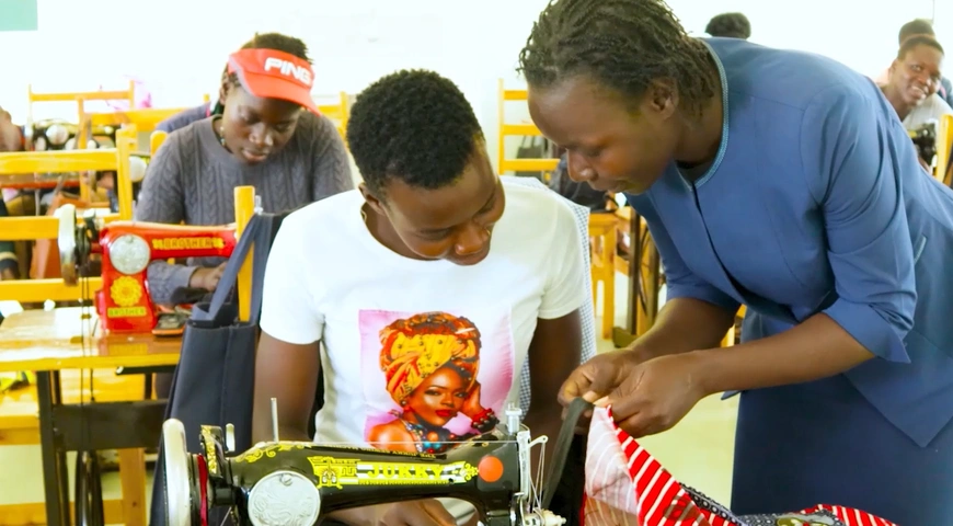 Mercy Odero explique quelque chose à une apprentie sur sa machine à coudre