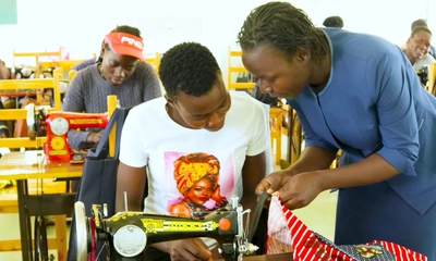 Mercy Odero explique quelque chose à une apprentie sur sa machine à coudre