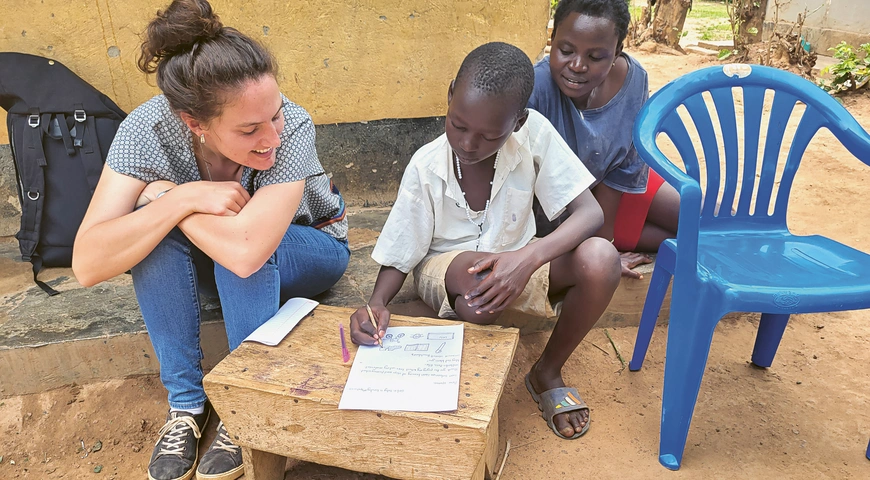 Varinia Dieperink, coopérante d’Eirene Suisse en Ouganda, avec un enfant dont l’écolage était financé par l’un des projets de YOLRED, en train d’écrire une lettre de remerciements.